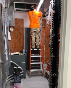 An electrician from Plains Electric on a ladder, working on complex wiring and electrical components in Auburn, AL.