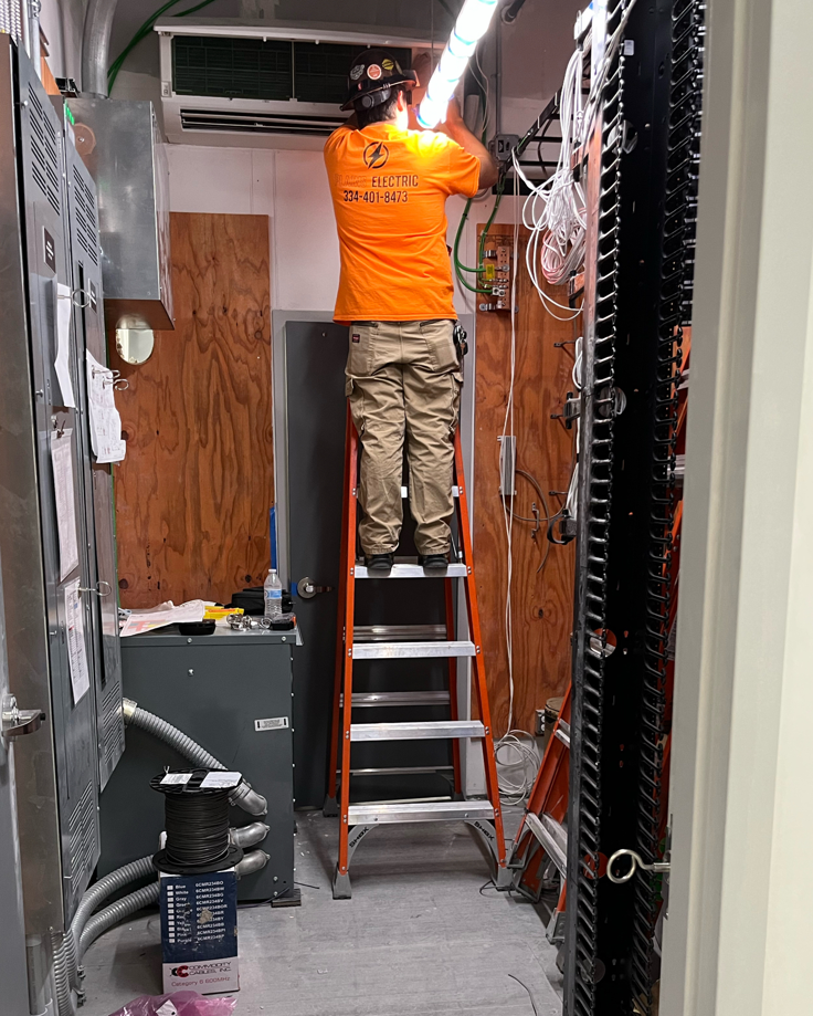 An electrician from Plains Electric on a ladder, working on complex wiring and electrical components in Auburn, AL.