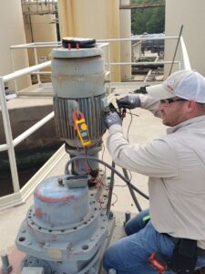 An electrician from Denali Electric LLC servicing an industrial motor with a multimeter in San Antonio, TX