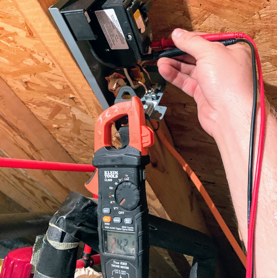 An electrician testing electrical wiring with a multimeter in an attic or crawl space for Joyner Electric And Security in Savannah, GA.