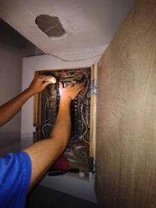 An electrician working on an open electrical panel with a flashlight, performing service for Pollock HVAC & Electrical in Albany, GA