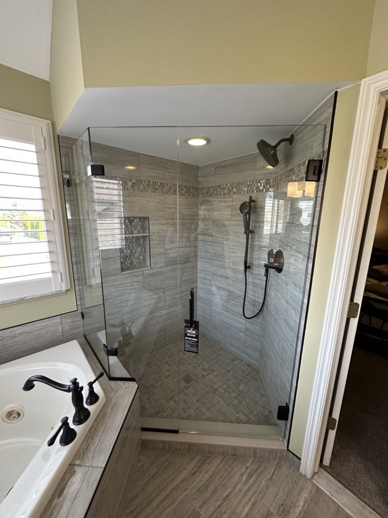 An elegant corner shower enclosure with grey tiled walls and a clear glass door by Fortune Shower Doors in Sterling Heights, MI.