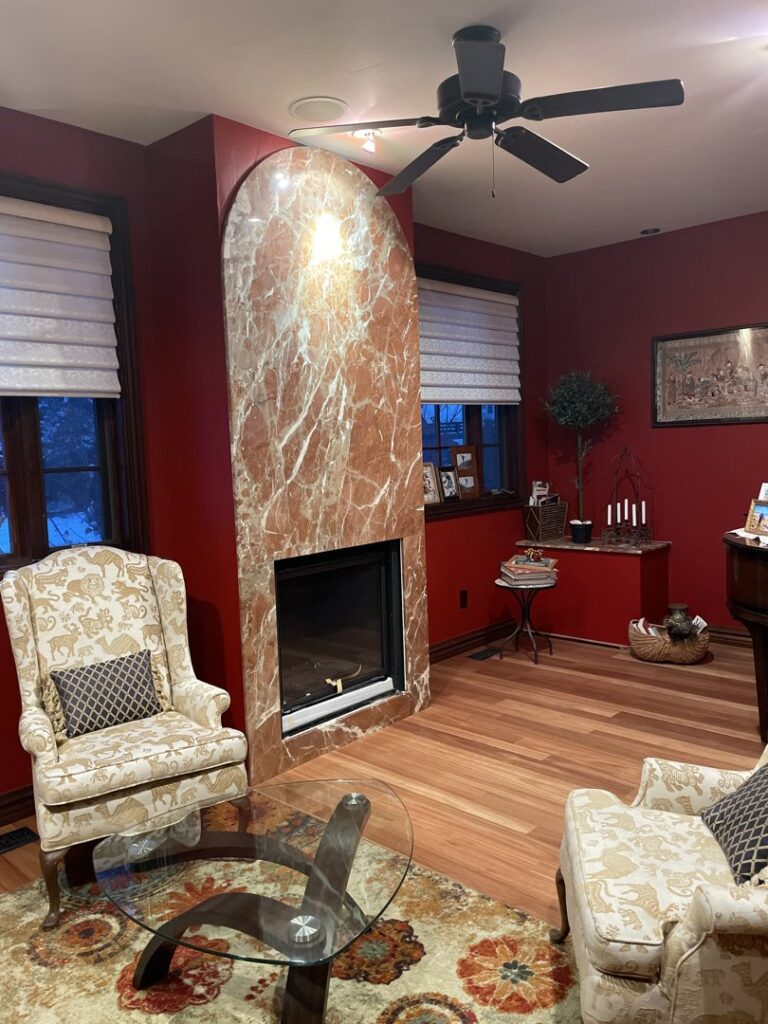 An elegant fireplace renovation with a marble-look surround in a room with red walls, completed by The Foundation Guys in Lakewood, CO