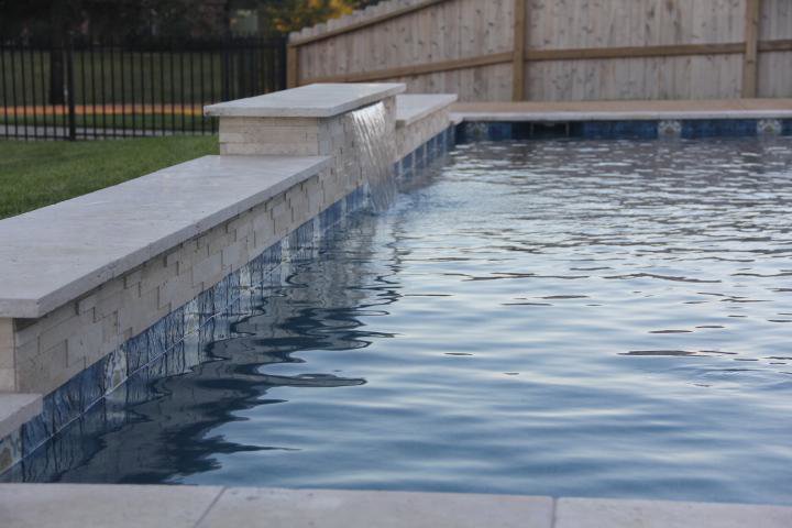 An elegant pool waterfall feature with stone coping, designed by Limitless Custom Pools and Backyards in Houston, TX.
