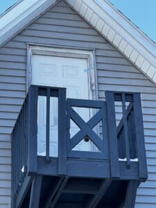 A newly constructed or repaired elevated wooden balcony with dark railings on a house by The Finish Group in Bangor, ME.