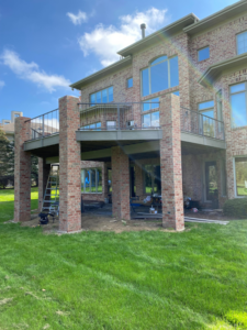 A large elevated deck supported by brick pillars, showing ongoing construction or recent completion by Nader Builders in Ann Arbor, MI.