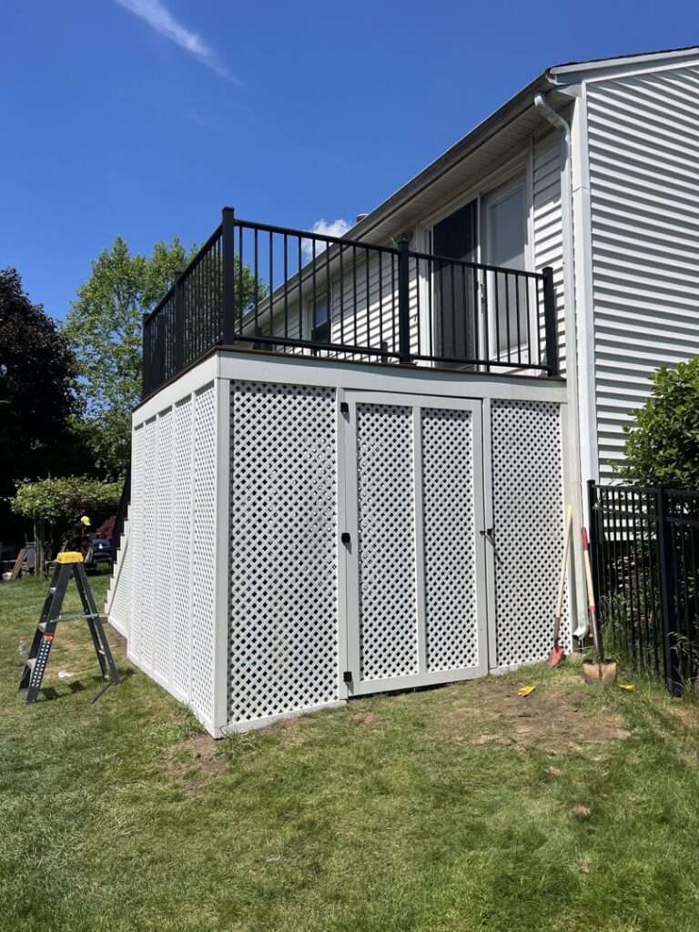 An elevated deck with white lattice skirting and black metal railings, a project completed by Men Construction in Lowell, MA.