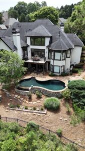 An elevated view of a large house with a custom swimming pool and extensive landscaping, a project by Picasso Poolscapes in Johns Creek, GA.