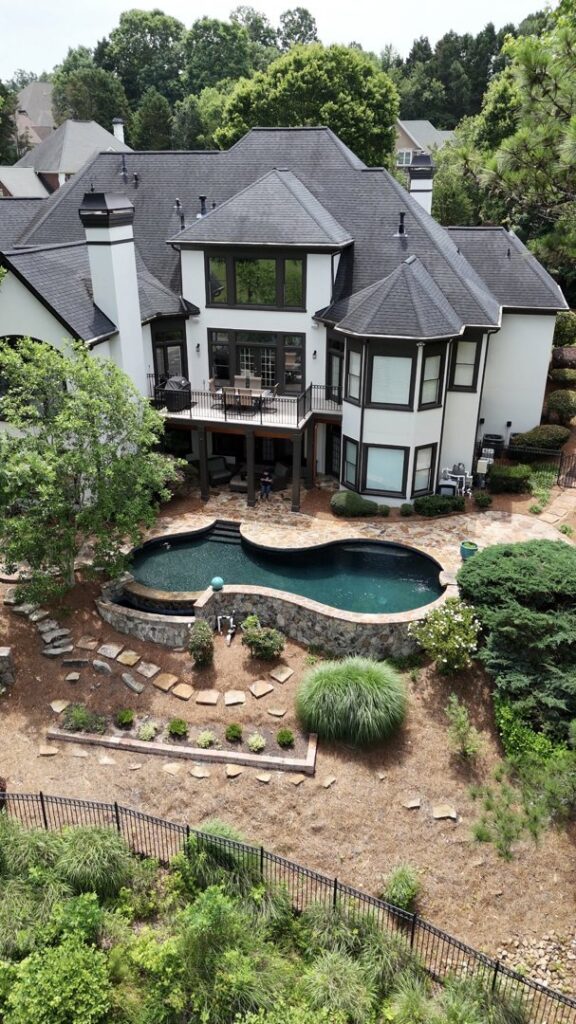 An elevated view of a large house with a custom swimming pool and extensive landscaping, a project by Picasso Poolscapes in Johns Creek, GA.