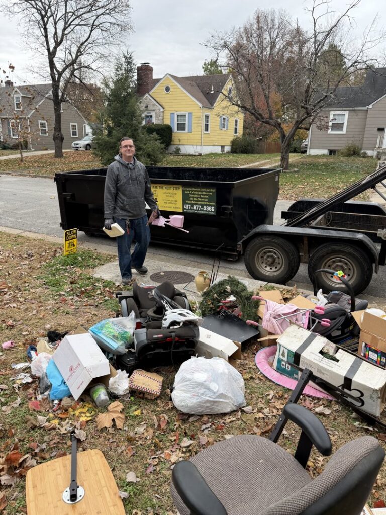 An employee standing next to a pile of household junk and a Waste Walkers Dispatch dumpster in Springfield, MO.