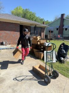 An LP Junk Removal employee carrying a wooden drawer, with other junk piled on a driveway in Birmingham, AL.
