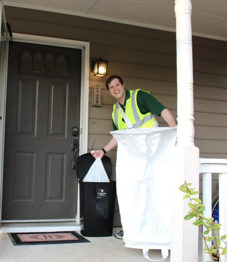 An A1 Valet Trash employee in Atlanta, GA, smiling while collecting a trash bag from a resident's doorstep.