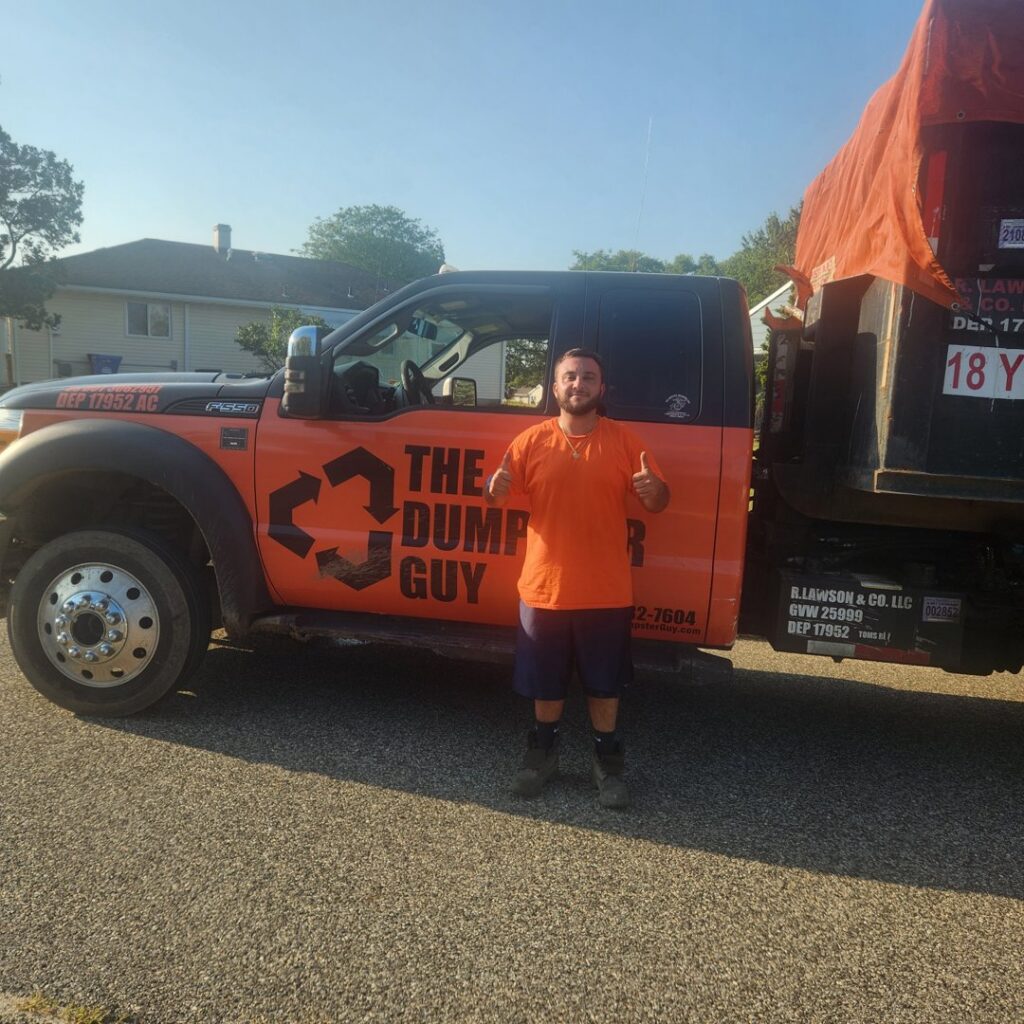 An employee of The Dumpster Guy giving a thumbs up next to a branded junk removal truck in Webster, MA.