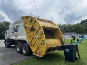 A One Waste Solutions employee emptying a blue trash bin into a garbage truck in Murfreesboro, TN, performing junk removal.