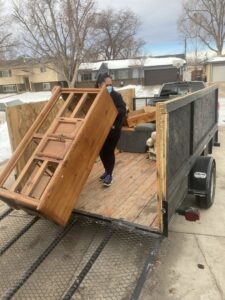 An employee loading a large wooden cabinet onto a trailer for Trash It All Hauling And Junk Removal LLC in Fort Collins, CO.