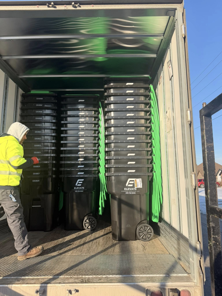 An employee loading black disposal bins into a truck for Elevate Disposal Services, LLC in Bentonville, AR