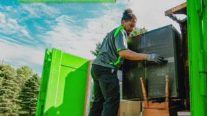 A Junkluggers employee loading a large item into a green junk removal truck for The Junkluggers in Hicksville, NY.