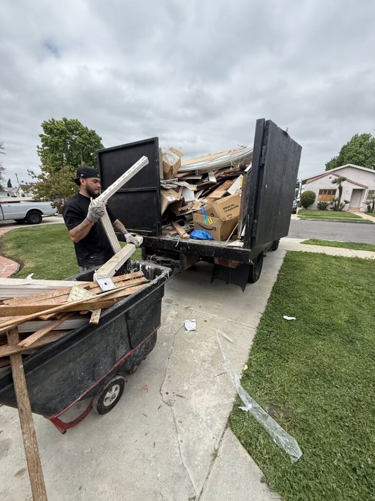 An L.A. Junk Squad employee loading wood debris from a cart into the back of a junk removal truck in Bell Gardens, CA.