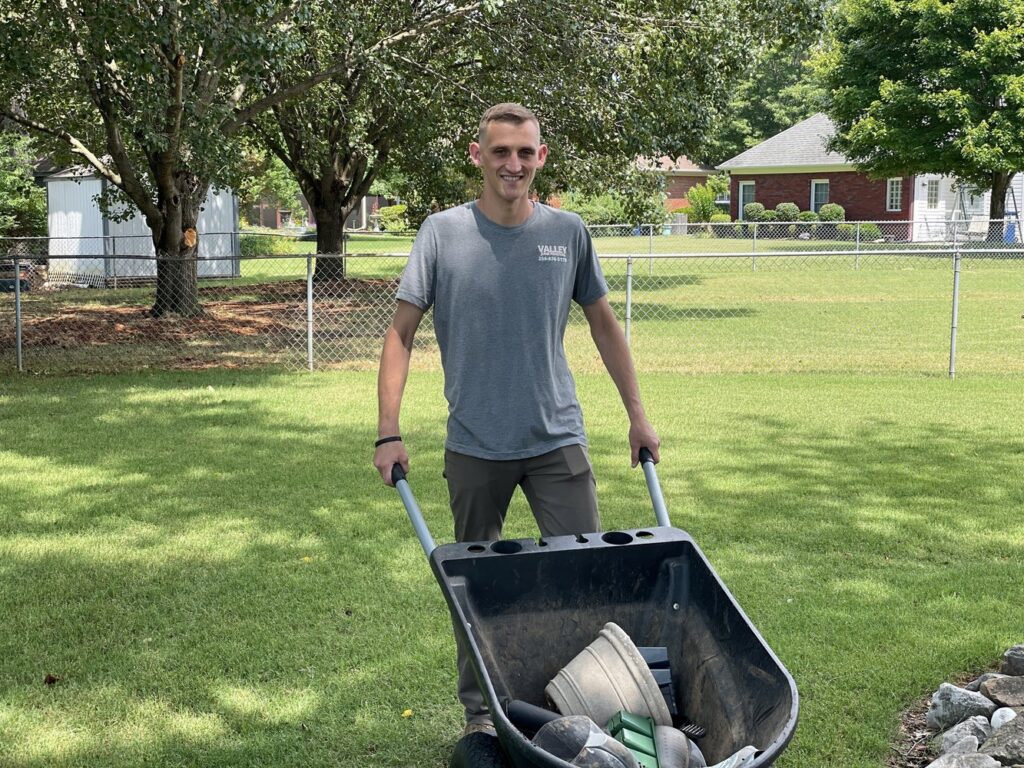A Valley Junk Removal employee pushing a wheelbarrow filled with items during a cleanup job in Huntsville, AL.