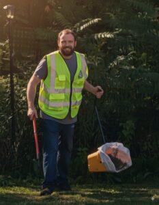 An employee of The Doo Doo Dudes in Lewiston, ME, scooping dog waste in a yard.