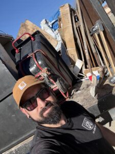 An L.A. Junk Squad employee taking a selfie in front of a truck bed loaded with various junk items in Bell Gardens, CA.