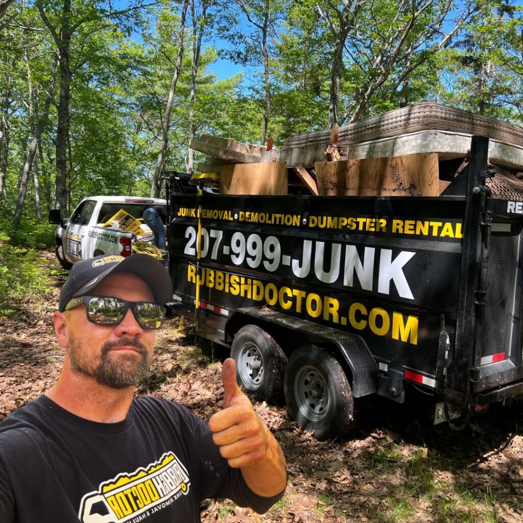 A Rubbish Doctor employee giving a thumbs up in front of a trailer filled with junk in Portland, ME.