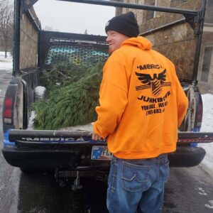 A Merica JunkBoss LLC employee standing by a truck bed containing a discarded Christmas tree, providing junk removal services in Hammond, IN.