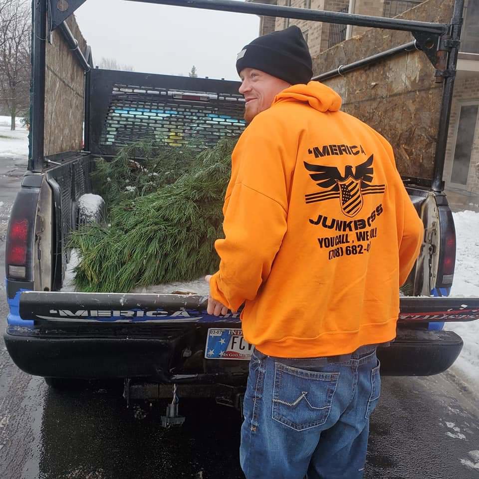 A Merica JunkBoss LLC employee standing by a truck bed containing a discarded Christmas tree, providing junk removal services in Hammond, IN.