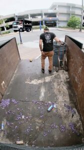 An L.A. Junk Squad employee with a dolly and trash can, standing inside an empty junk removal truck bed in Bell Gardens, CA.