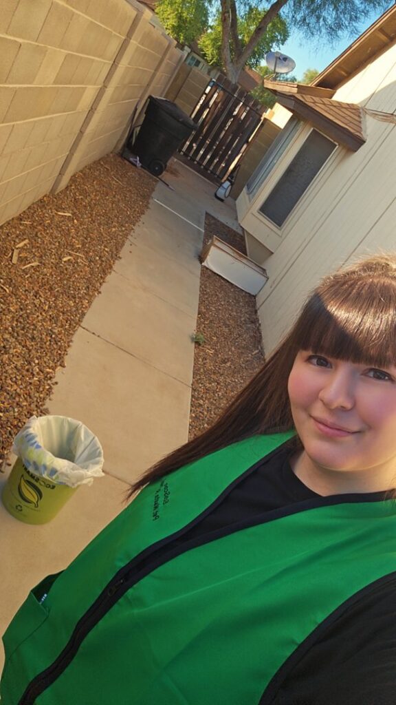 An EcoScoops Pet Waste Removal employee in a green vest with an EcoSmart bucket in the background, ready for service in Gilbert, AZ.