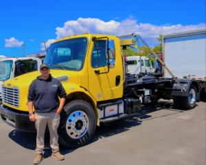 An employee stands next to a yellow roll-off truck chassis, representing Mac's Disposal LLC's junk removal services in Kenosha, WI.