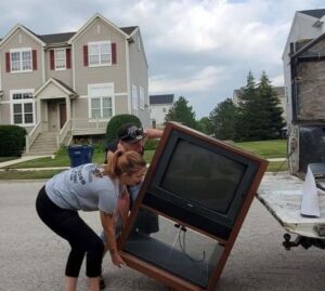 Two Merica JunkBoss LLC employees loading a large old television into the back of a junk removal truck, performing a job in Hammond, IN.