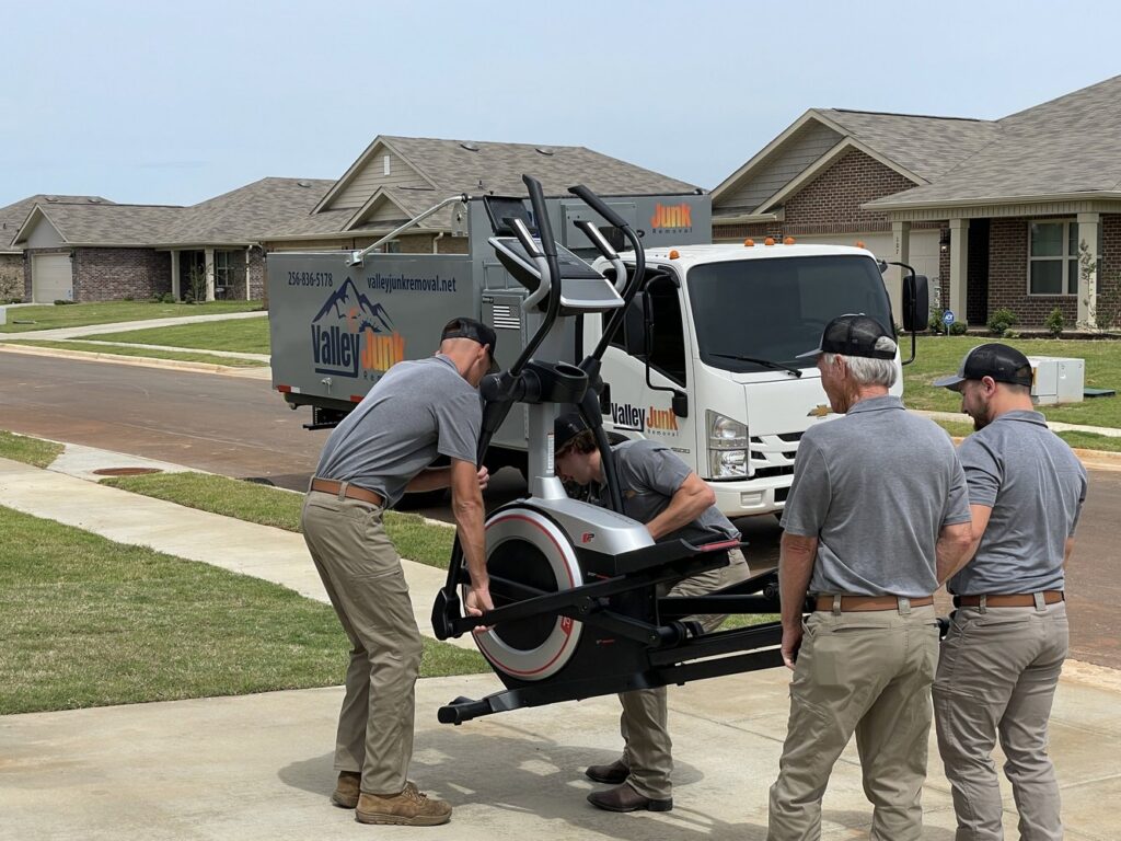 Valley Junk Removal employees carefully removing a large elliptical machine and loading it onto their truck in Huntsville, AL.