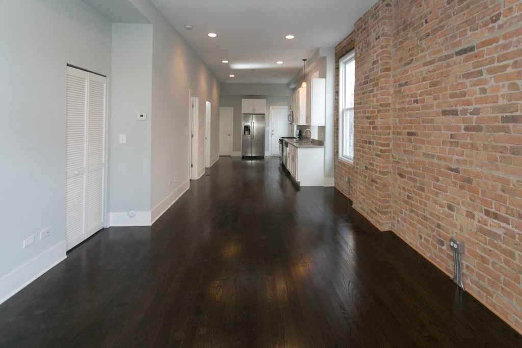 An empty apartment interior with dark wood floors and an exposed brick wall, renovated by 3F Construction in Chicago, IL.
