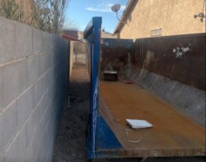 An empty blue dumpster placed in a narrow alleyway, ready for junk removal or cleanout services from Massie Dumpster Rental in Las Vegas, NV.