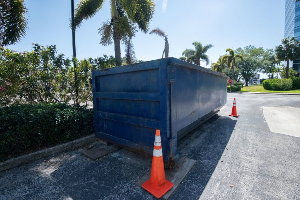 An empty blue roll-off dumpster with orange traffic cones, placed for junk removal by Waste Master Dumpster Rental Orlando, FL.