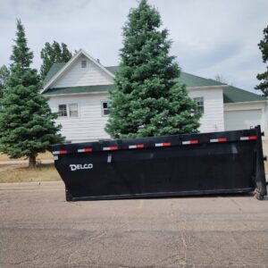 An empty DELCO dumpster parked in front of a house for junk removal by T-Rex Service LLC in Cheyenne, WY.