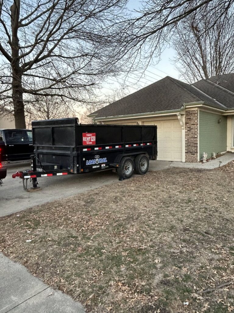 An empty black dump trailer from D's Dumpster Rentals parked in a residential driveway in Overland Park, KS.