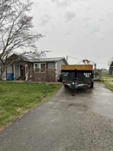 An empty dump trailer with wooden extensions parked on a driveway in front of a residential house from Salt Creek Disposal in Bowling Green, KY.