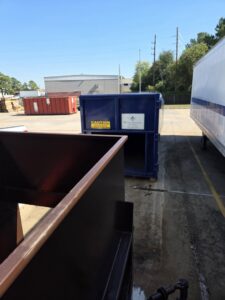 An empty brown dumpster with other Waste Connections commercial and roll-off dumpsters visible in the background in Houston, TX.