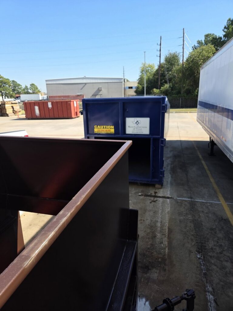 An empty brown dumpster with other Waste Connections commercial and roll-off dumpsters visible in the background in Houston, TX.