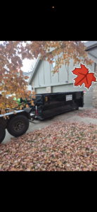 An empty H & H Dumpster Rental dumpster on a leaf-covered driveway in Rootstown, OH, ready for fall cleanup.