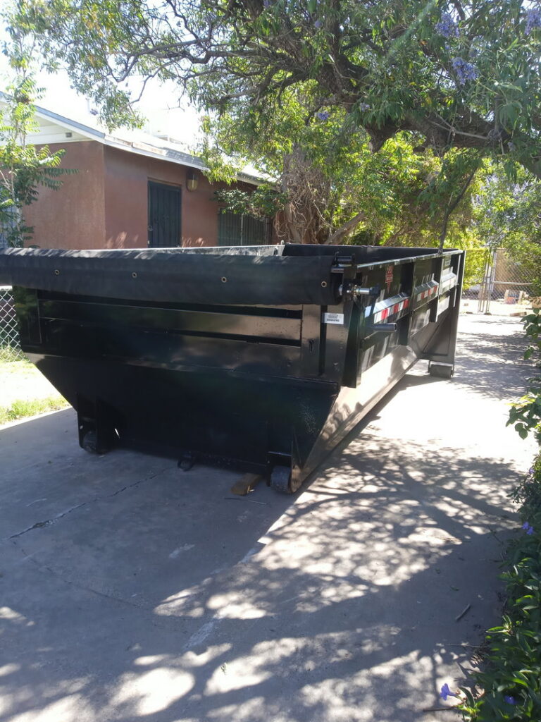 An empty black dumpster parked in front of a house, ready for junk removal by Construction Removal Services Inc. in El Paso, TX.