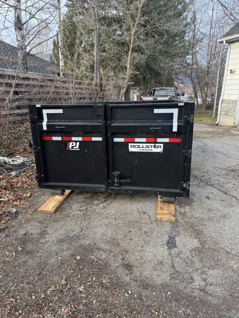 An empty DumpsterDash-LLC dumpster in Ogden, UT, placed on a gravel driveway, ready for junk removal.