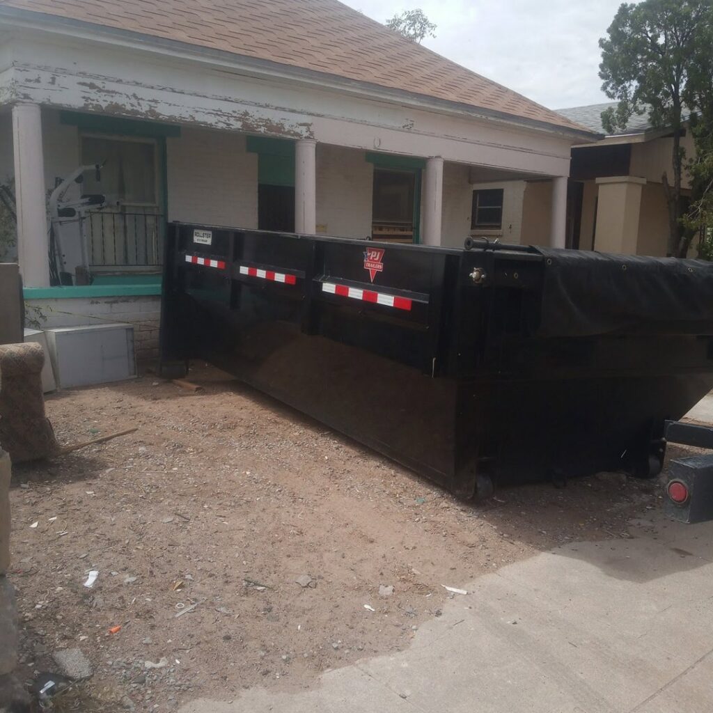 An empty black dumpster placed on a residential driveway for junk removal by Construction Removal Services Inc. in El Paso, TX.