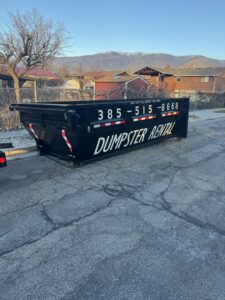 An empty DumpsterDash-LLC dumpster in Ogden, UT, parked on a residential street, ready for junk removal.