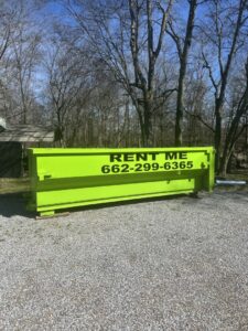An empty bright green dumpster placed in a gravel area for rental by Tristate Dumpsters LLC in Greenville, MS.