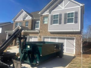 An empty green dumpster being delivered or picked up from a residential driveway by Beetles Dumpsters Rental & Junk Removal in Huntsville, AL.