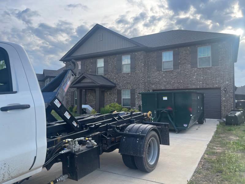 An empty green dumpster being delivered or picked up from a residential driveway by Beetles Dumpsters Rental & Junk Removal in Huntsville, AL.