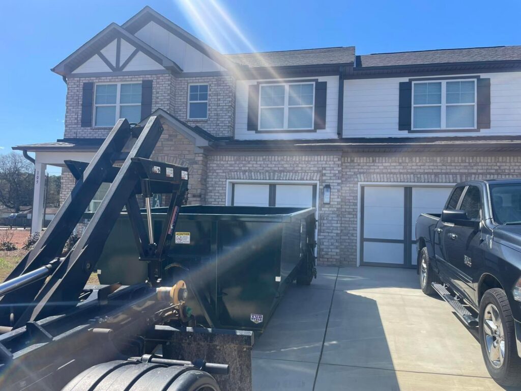 An empty green dumpster being delivered or picked up from a residential driveway by Beetles Dumpsters Rental & Junk Removal in Huntsville, AL.